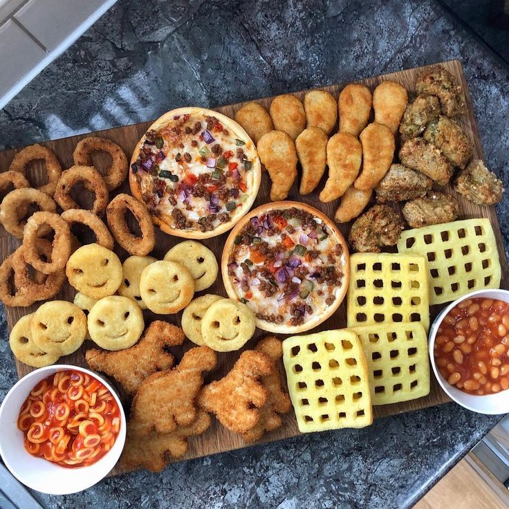 an assortment of food is displayed on a wooden platter with bowls of sauces and pretzels