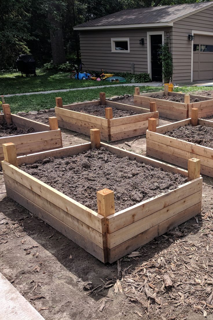 several wooden raised garden beds with dirt on the ground in front of a house and yard