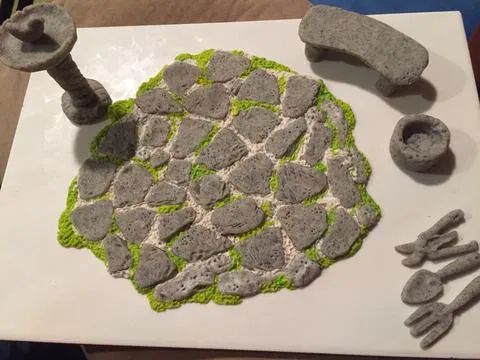 an art project made out of rocks and cements on a white board with green accents