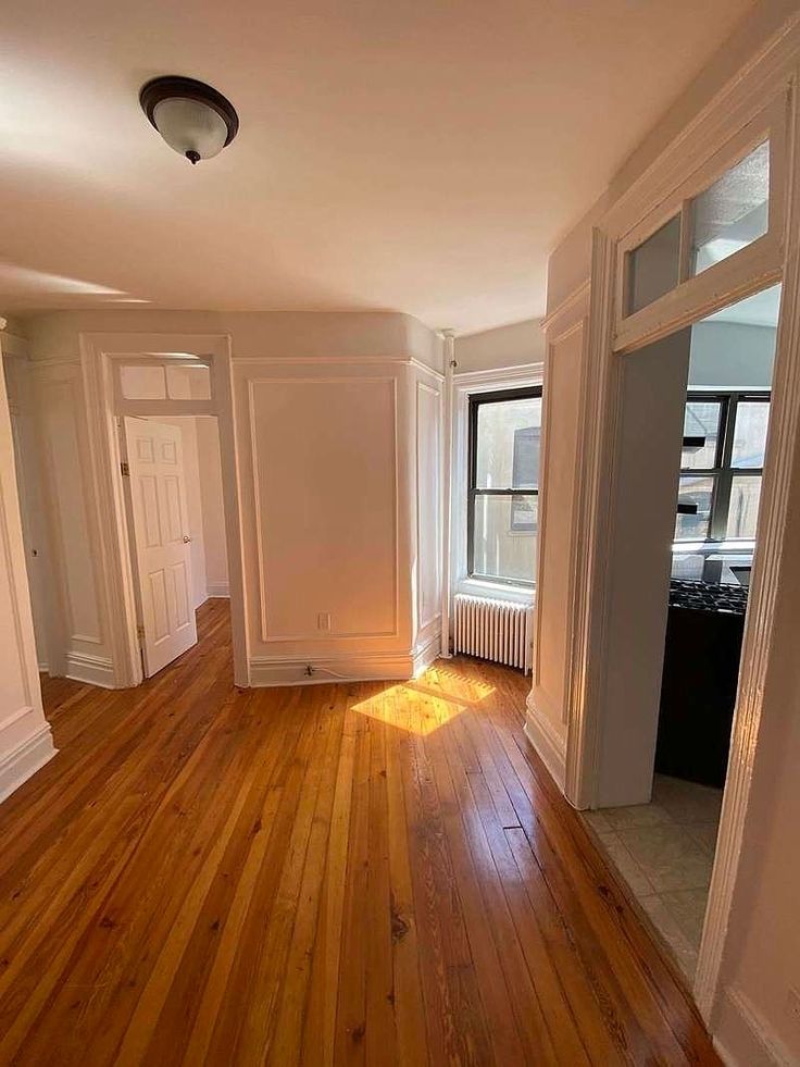 an empty room with hard wood flooring and white walls, windows, and doors