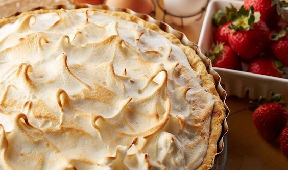 a pie sitting on top of a wooden table next to some strawberries and eggs