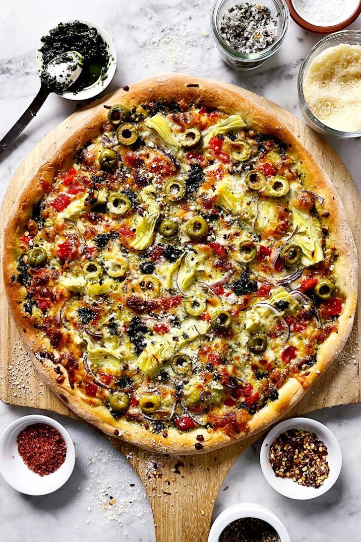 a pizza sitting on top of a wooden cutting board next to bowls and spoons