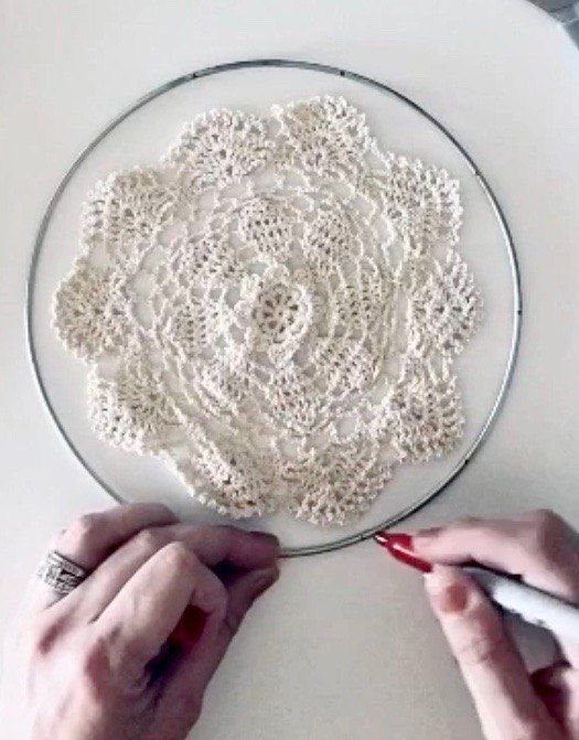 two hands crocheting a doily on a glass plate with red nail polish