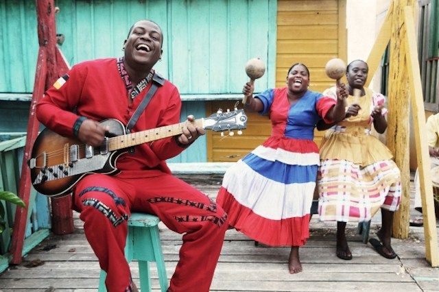 three people are sitting on the porch playing instruments and singing while one woman is holding a guitar