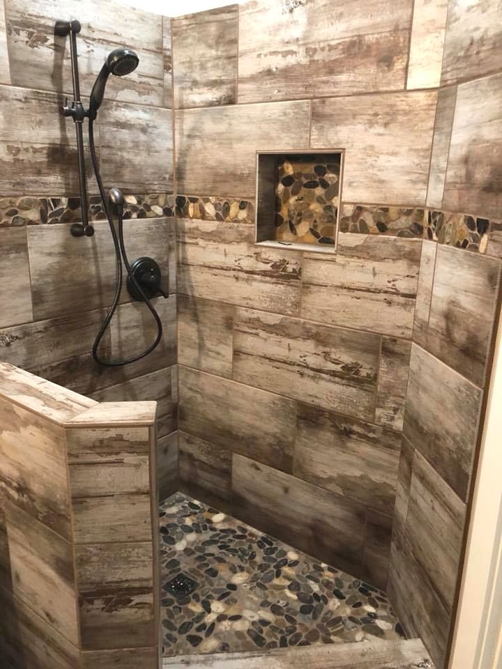 a walk in shower sitting next to a wooden wall and tiled floor with rocks on the ground