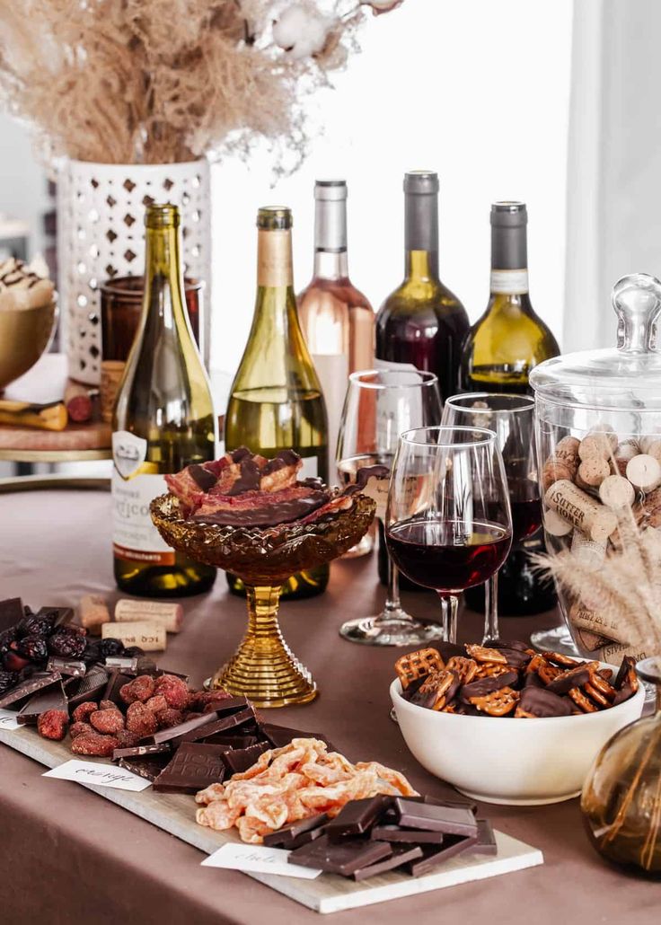 a table topped with wine bottles and glasses filled with different types of food, snacks and desserts