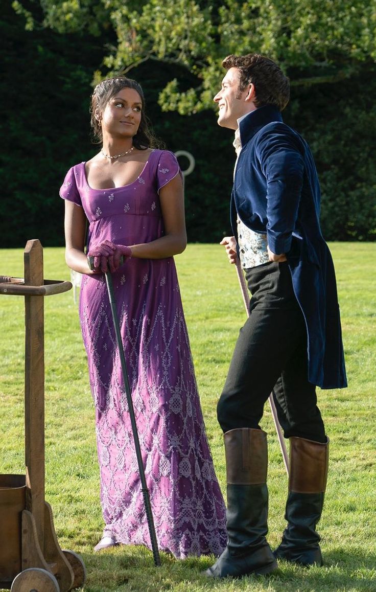 a man and woman dressed in period clothing standing next to each other on the grass