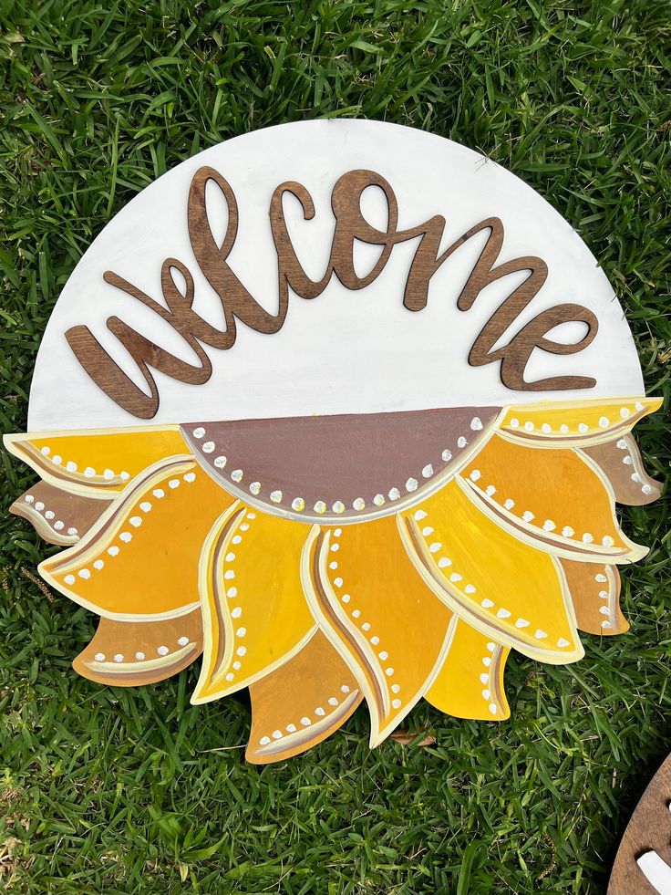 a welcome sign is on the grass with shoes in the foreground and someone's feet standing next to it