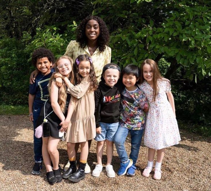 a group of children standing next to each other in front of some bushes and trees