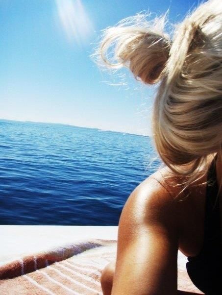 a woman sitting on top of a boat looking out at the ocean with her hair blowing in the wind