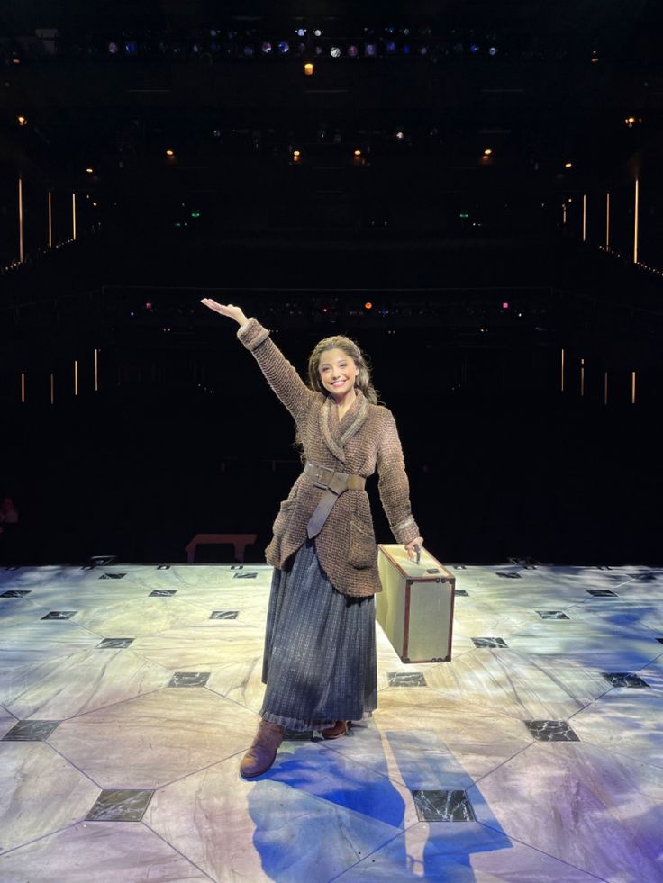 a woman holding a suitcase and pointing to the sky on stage with her hand in the air