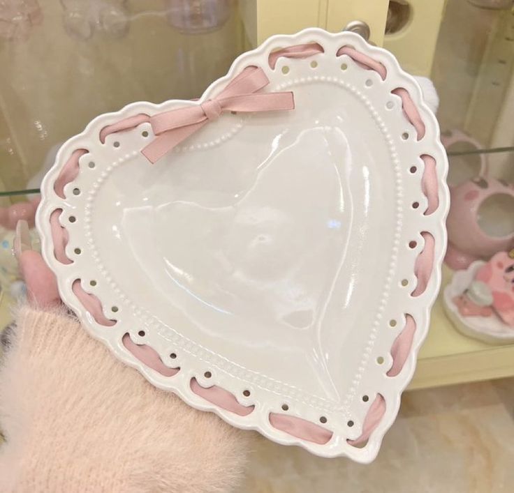 a pink teddy bear holding a heart shaped plate in front of a display case with other items