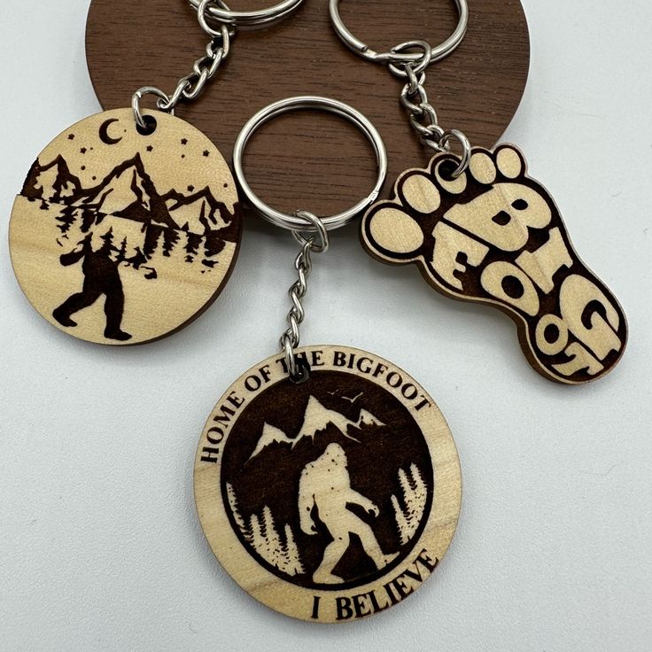 three wooden key chains with the words land of the bigfoot and a bear