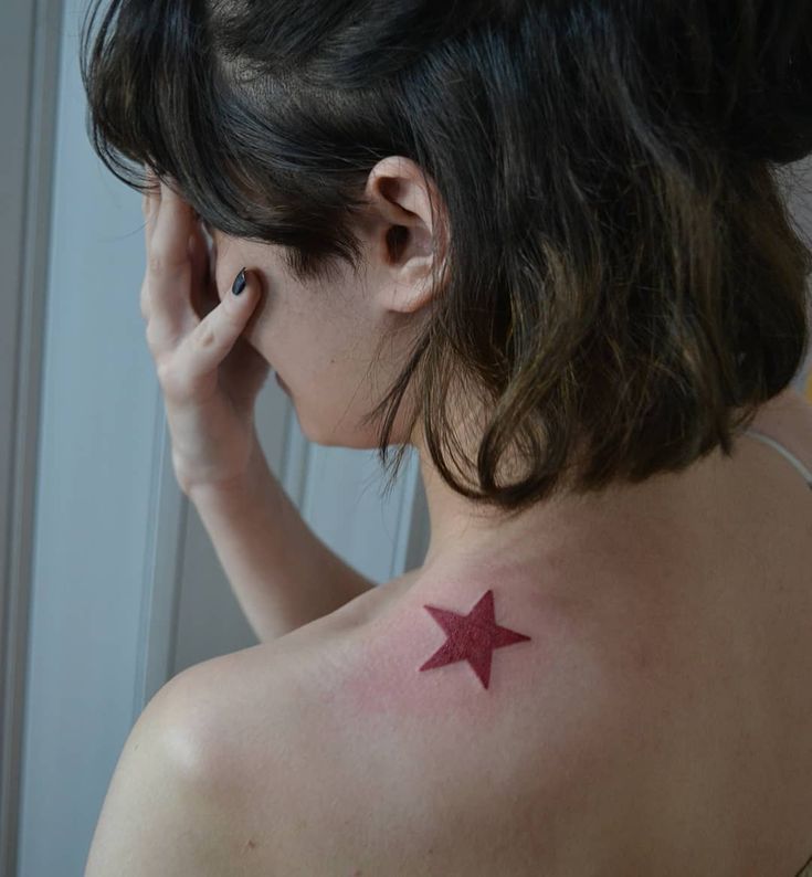 a woman with a red star tattoo on her upper back shoulder and behind her ear