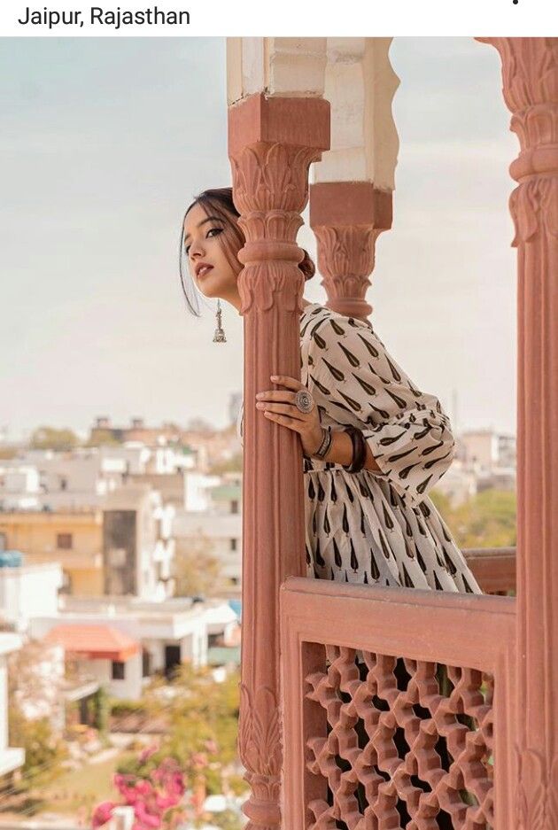 a woman standing on top of a balcony next to a tall pillar and wearing a black and white dress