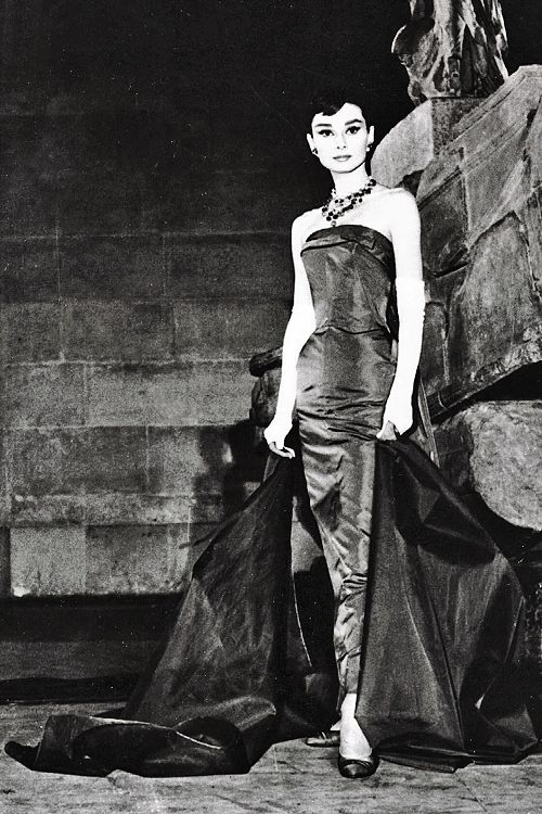 a black and white photo of a woman in a dress on the catwalk with luggage behind her