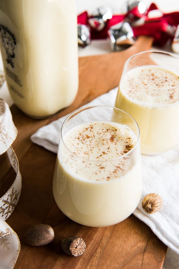 two glasses filled with white liquid sitting on top of a wooden table next to a bottle of milk