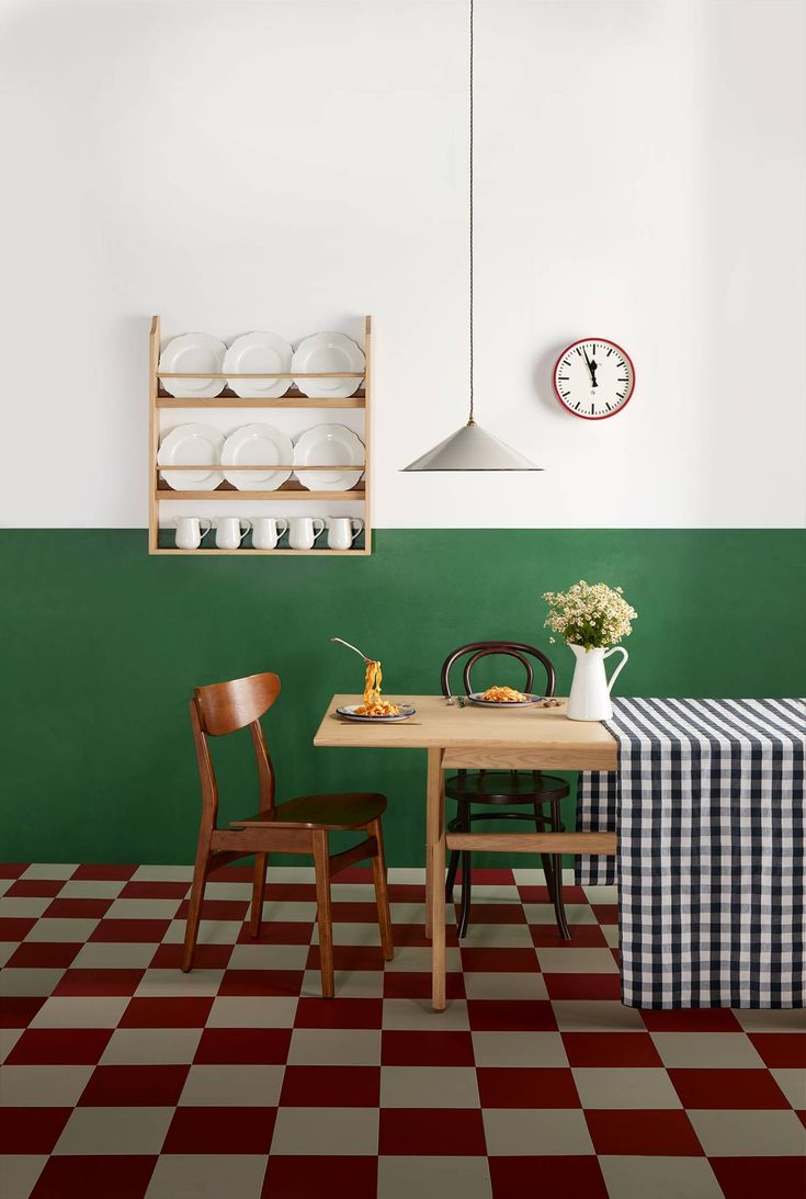 a dining room with green walls and checkered table cloth on the floor, two wooden chairs