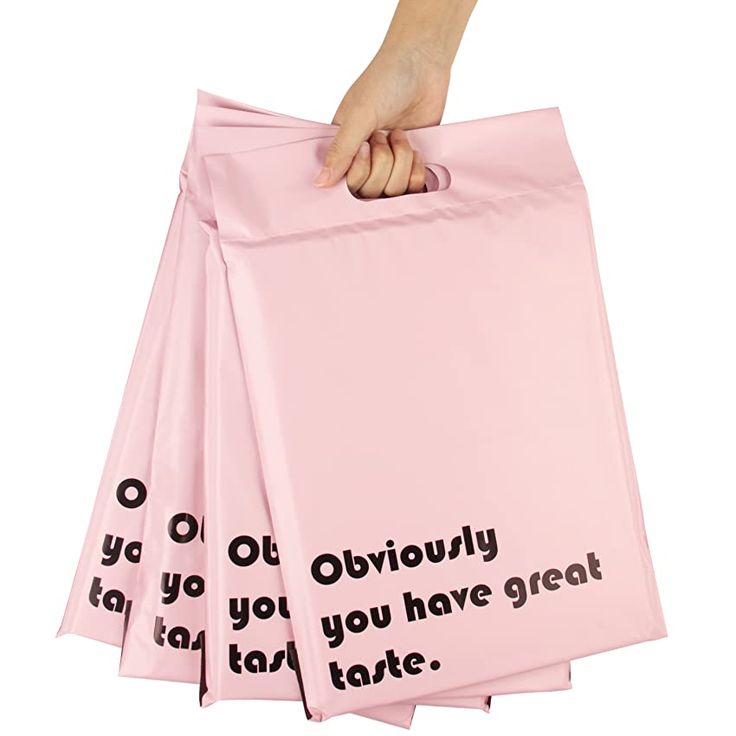 a hand holding a pink shopping bag with words on it