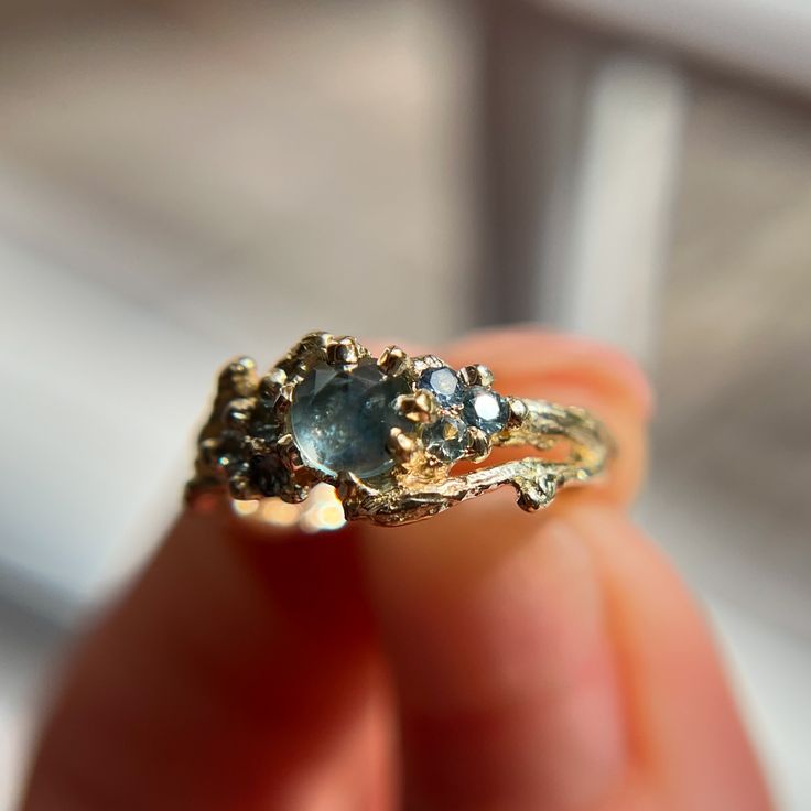 a close up of a person's hand holding a gold ring with an aqua blue stone