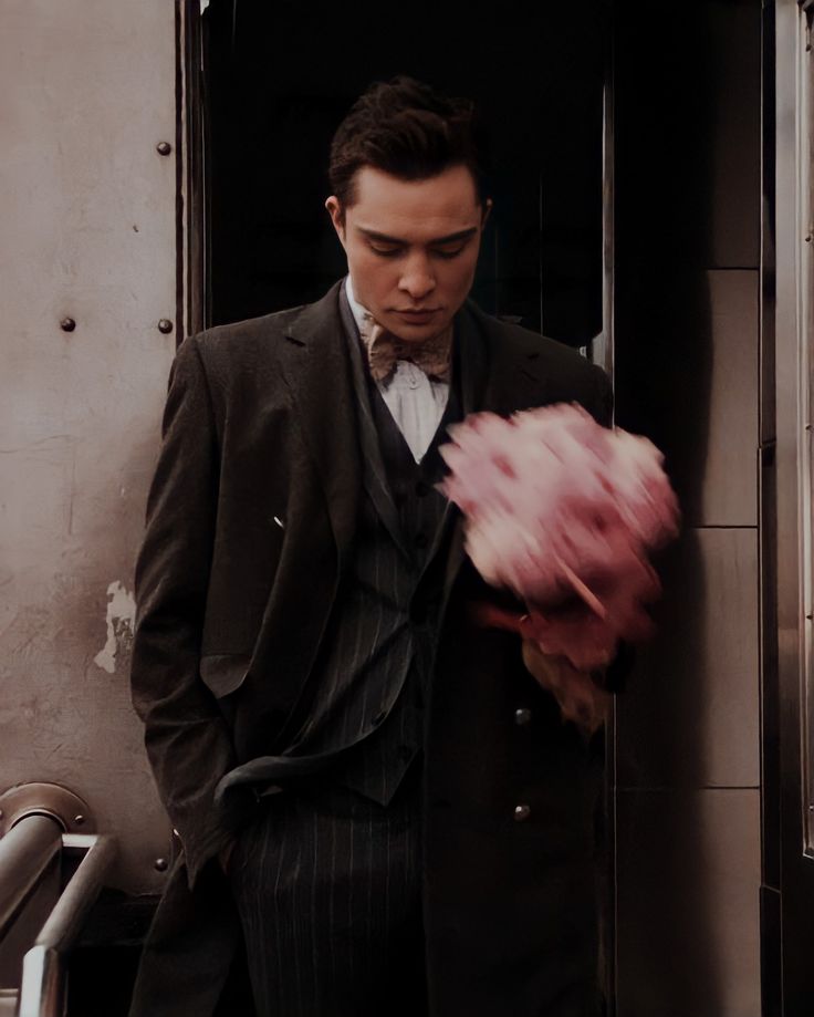 a man in a suit and tie holding a bouquet of pink flowers while standing next to a train