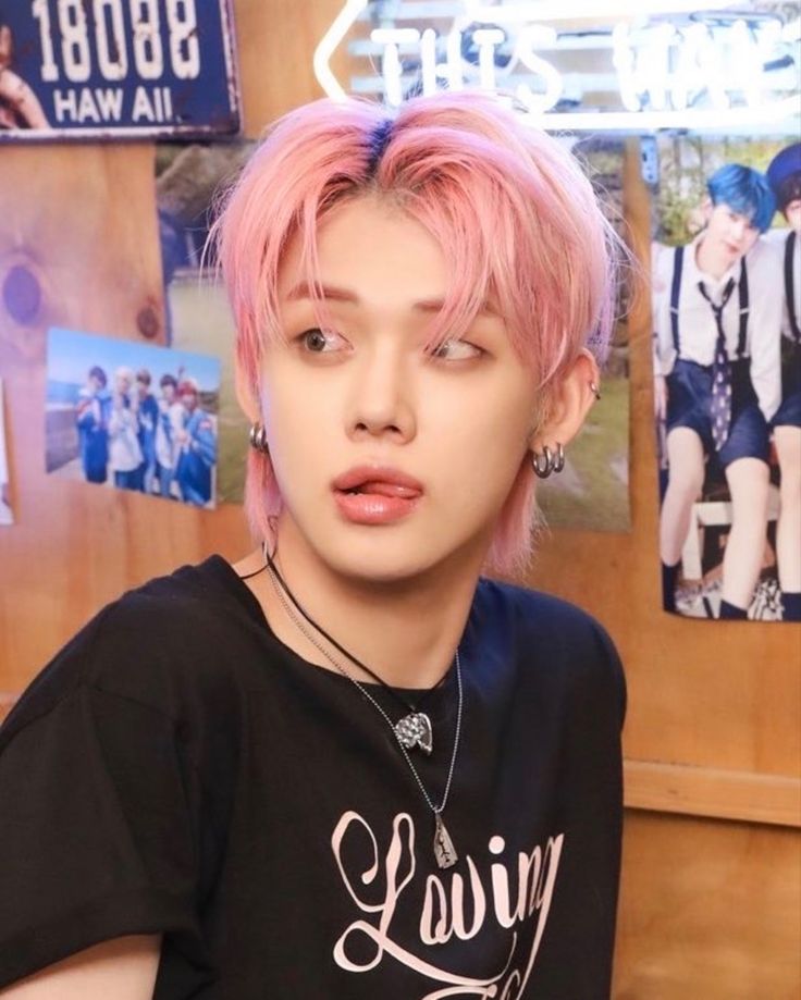 a young man with pink hair wearing a black t - shirt and silver earrings