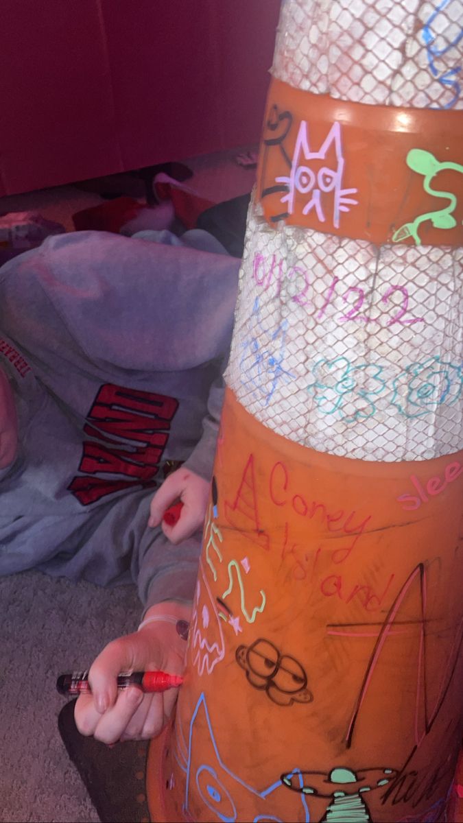 a child is writing on an orange traffic cone with lots of letters and numbers painted all over it