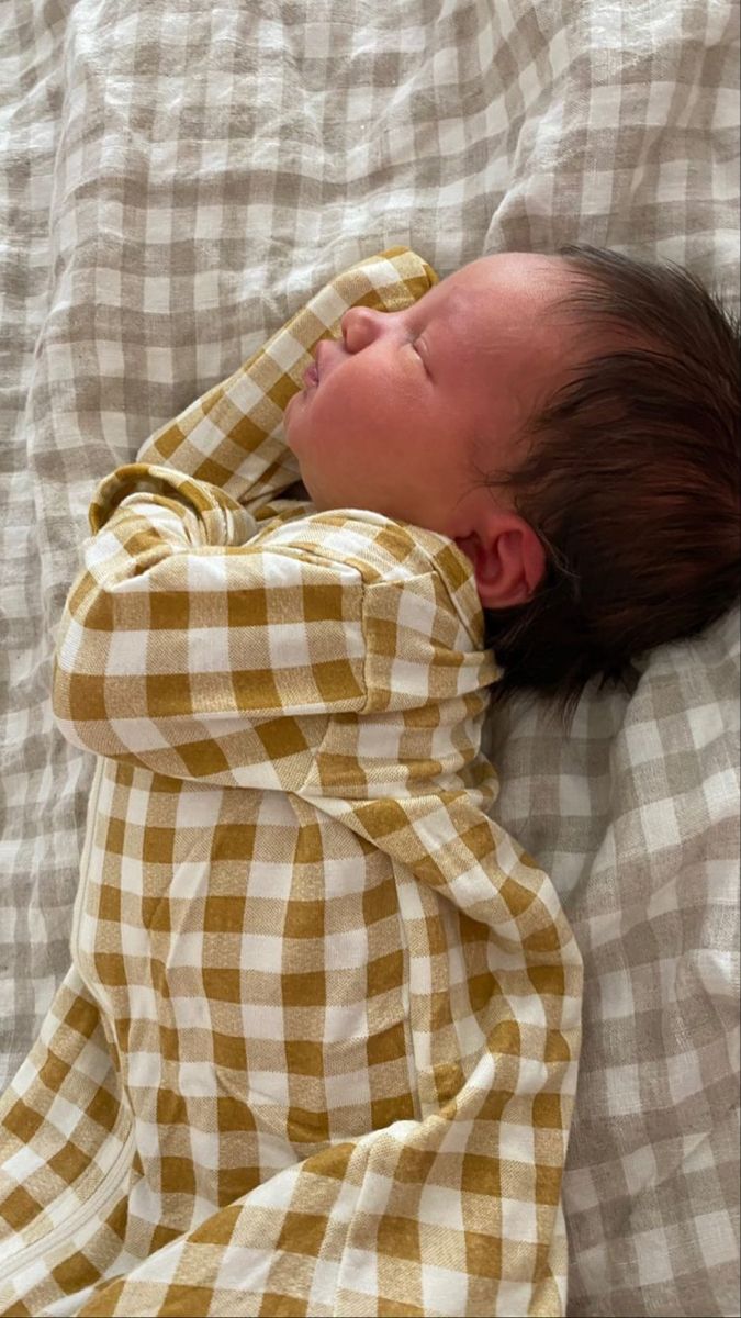 a baby is sleeping on a bed with a checkered cover over it's head