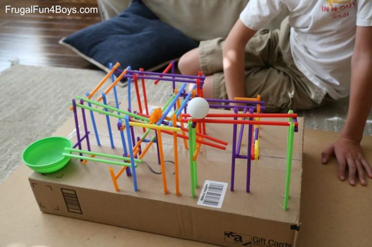 a young boy sitting on the floor next to a cardboard box filled with construction toys