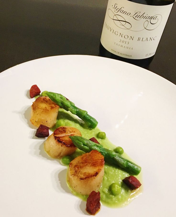 a white plate topped with scallops and asparagus next to a bottle of wine