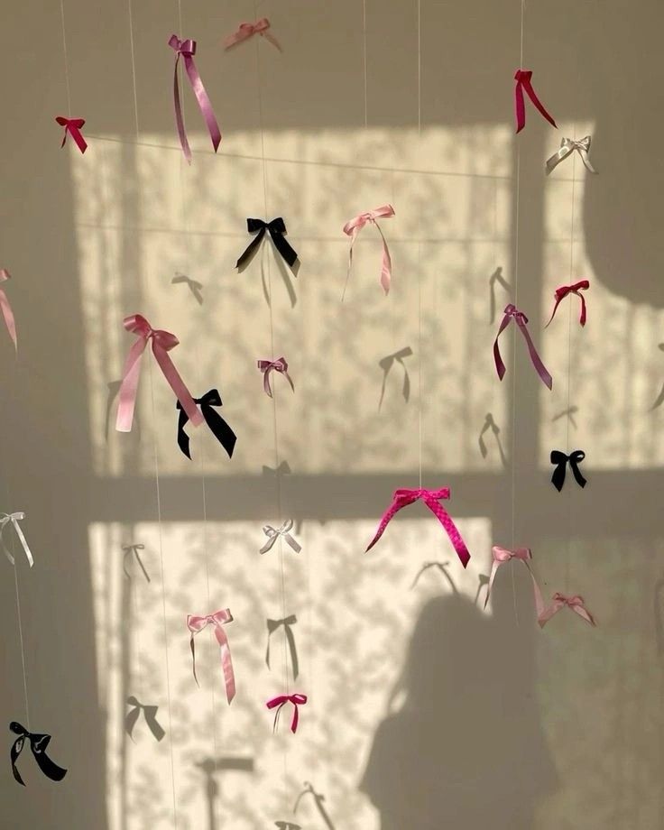 some pink and black ribbons are hanging from the ceiling in front of a white wall