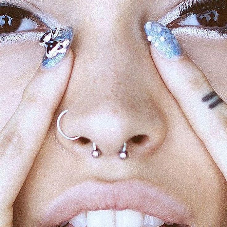 a close up of a woman with piercings on her nose and hands covering her eyes