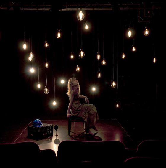 a woman sitting on a chair in front of a stage with lights hanging from the ceiling