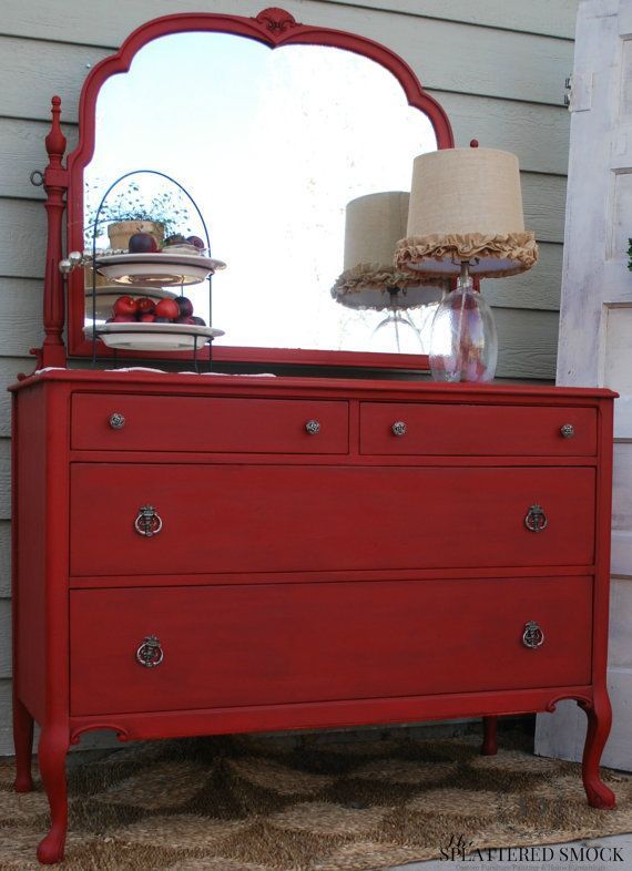 a red dresser with a mirror and lamp on it's top shelf in front of a house