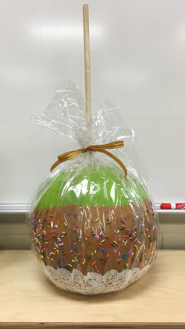 a green apple wrapped in plastic with sprinkles and a wooden stick sticking out of it