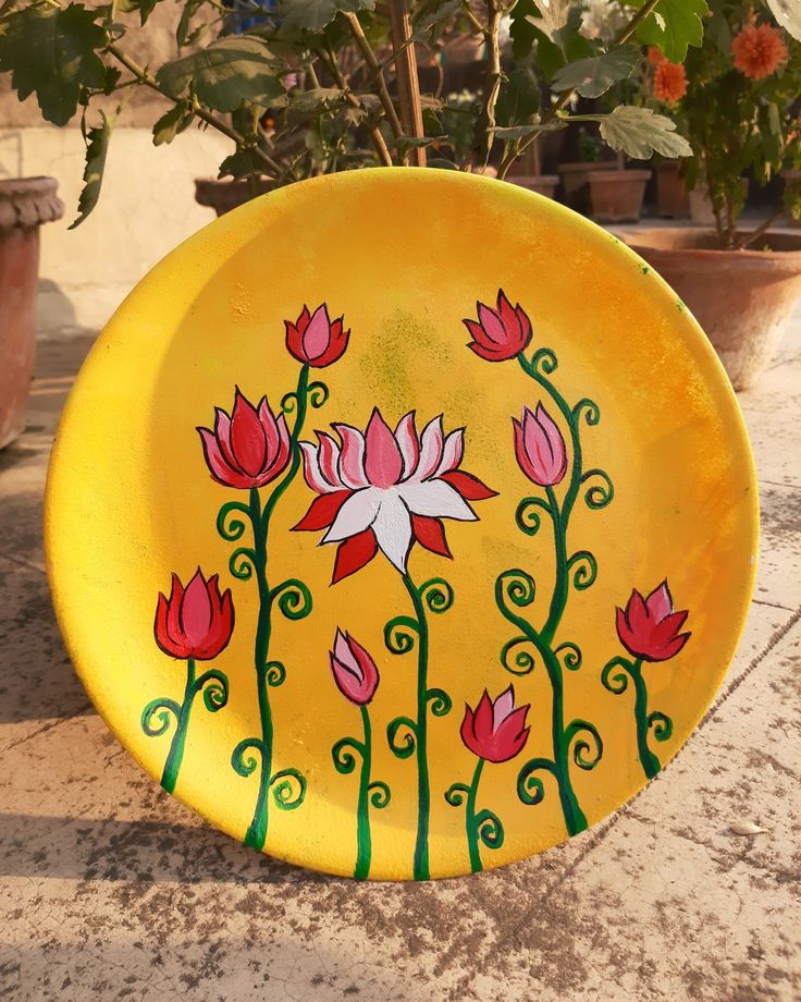 a yellow plate with flowers painted on it sitting in front of some potted plants