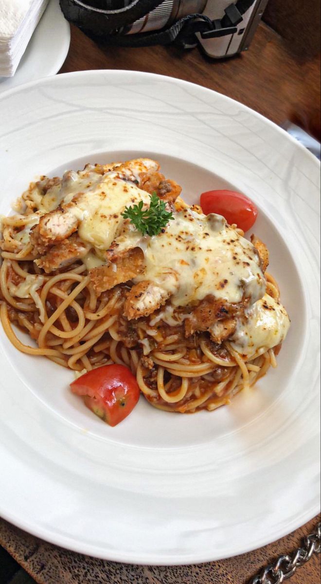 a white plate topped with pasta and meat covered in sauce on top of a wooden table