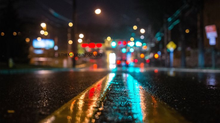 a wet street at night with lights reflecting off the wet pavement and buildings in the background