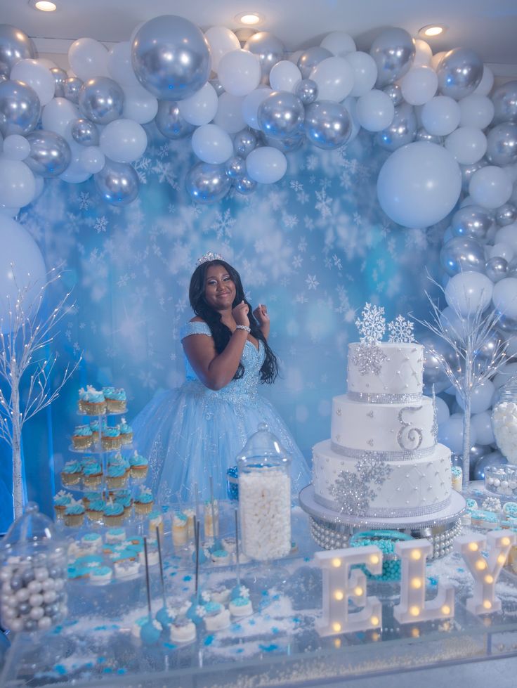 a woman standing in front of a cake surrounded by white and blue desserts with snowflakes