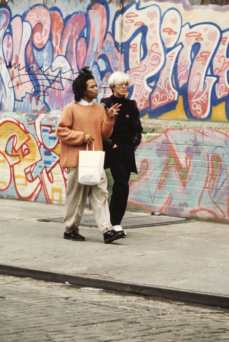 two women walking down the street in front of graffiti