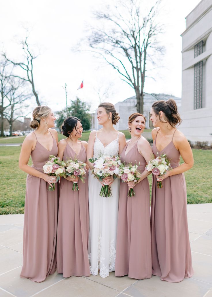 a group of women standing next to each other in front of a building holding bouquets