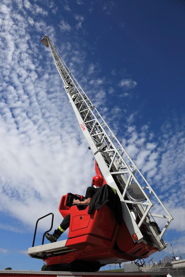 a man sitting on top of a red truck under a blue sky with wispy clouds