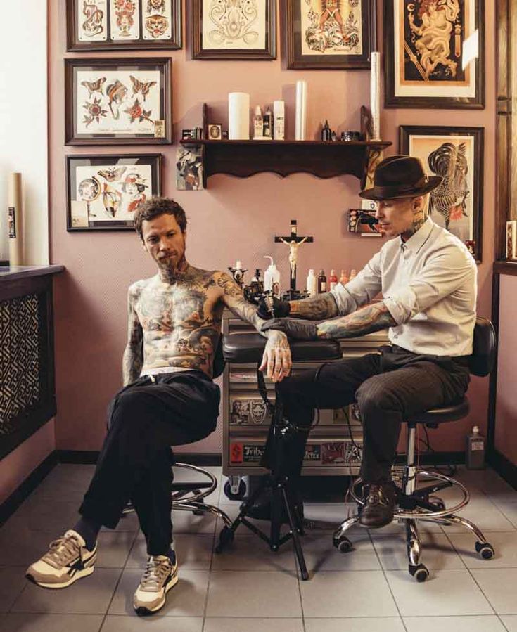 two men sitting at a barbershop with tattoos on their arms and chests