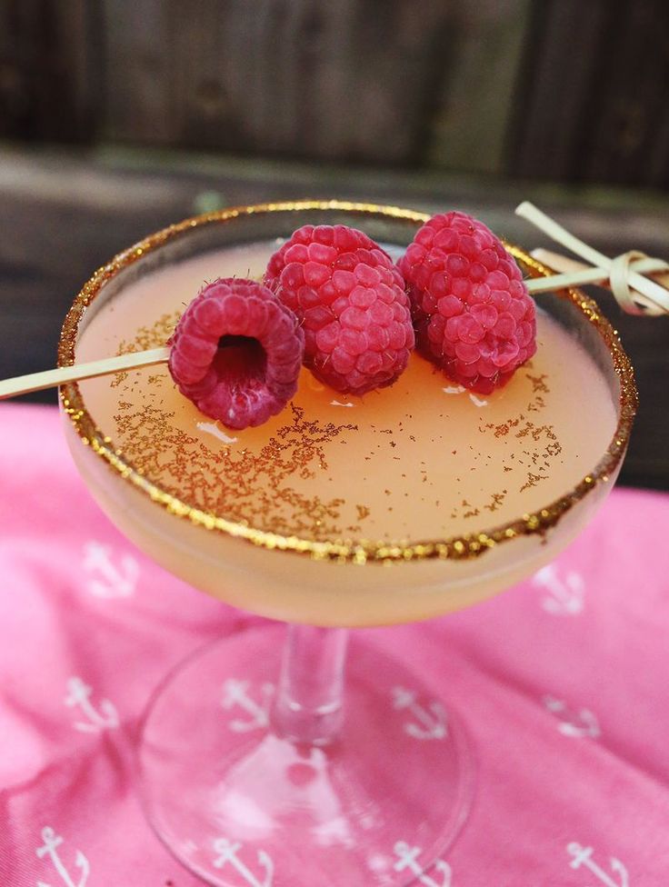 raspberries sit on top of a drink in a glass with gold rims