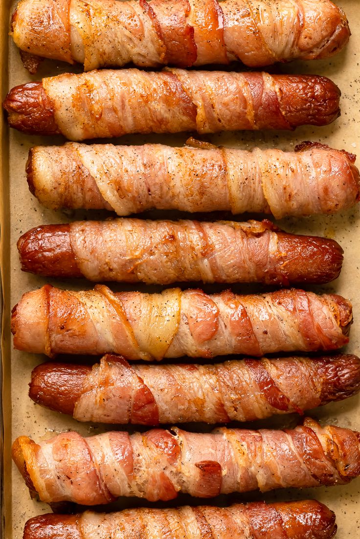 bacon wrapped hotdogs are lined up on a baking sheet and ready to be eaten