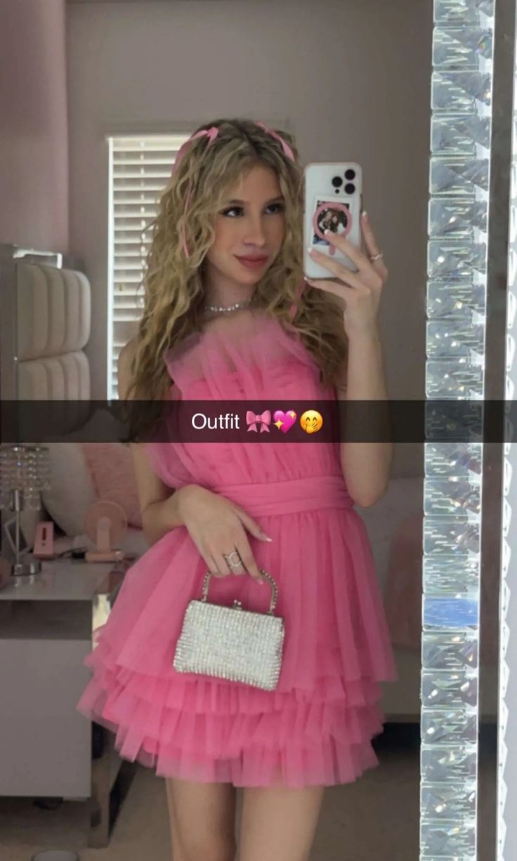 a woman in a pink dress taking a selfie with her cell phone and purse