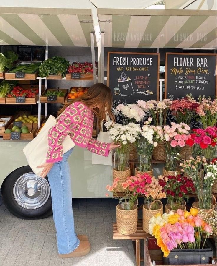 a woman standing in front of a food truck filled with fresh flowers and plants for sale