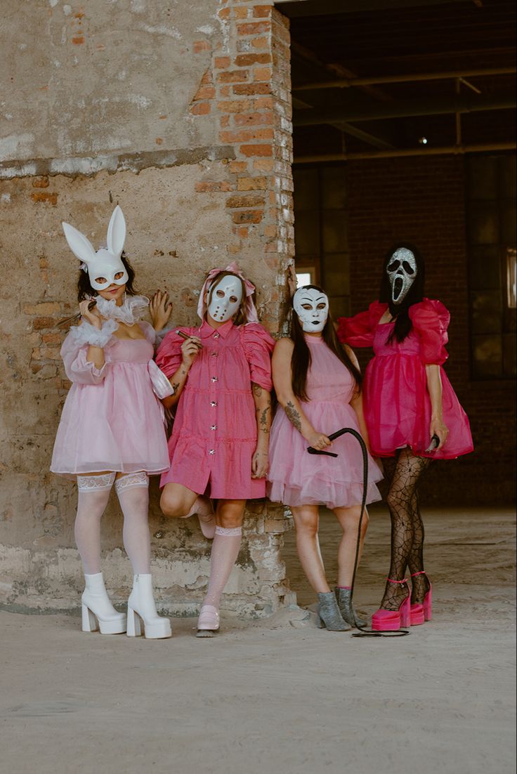 three women in pink dresses and masks standing next to each other near a brick wall