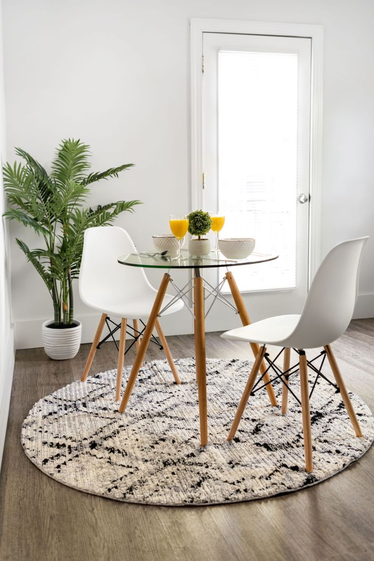 a glass table with two chairs and a potted plant in the corner next to it