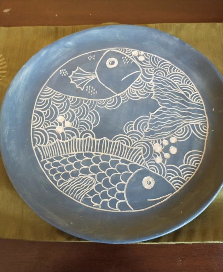 a blue plate with fish on it sitting on a wooden table next to a fan